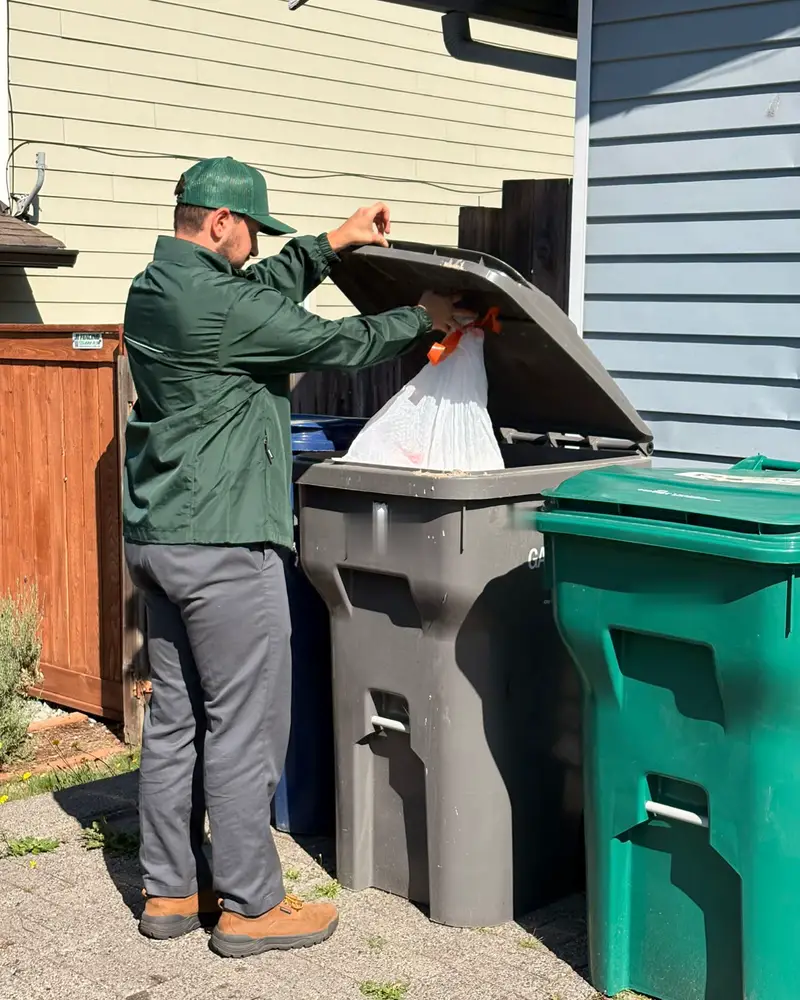 Doody Free scooper placing a tied, double-bagged sack of dog waste into a customer's outdoor trash bin
