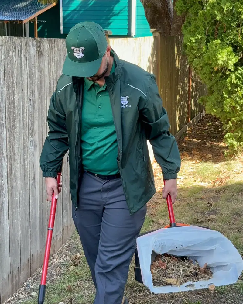 A Doody Free scooper in the green company uniform working along a fence line in a Federal Way yard